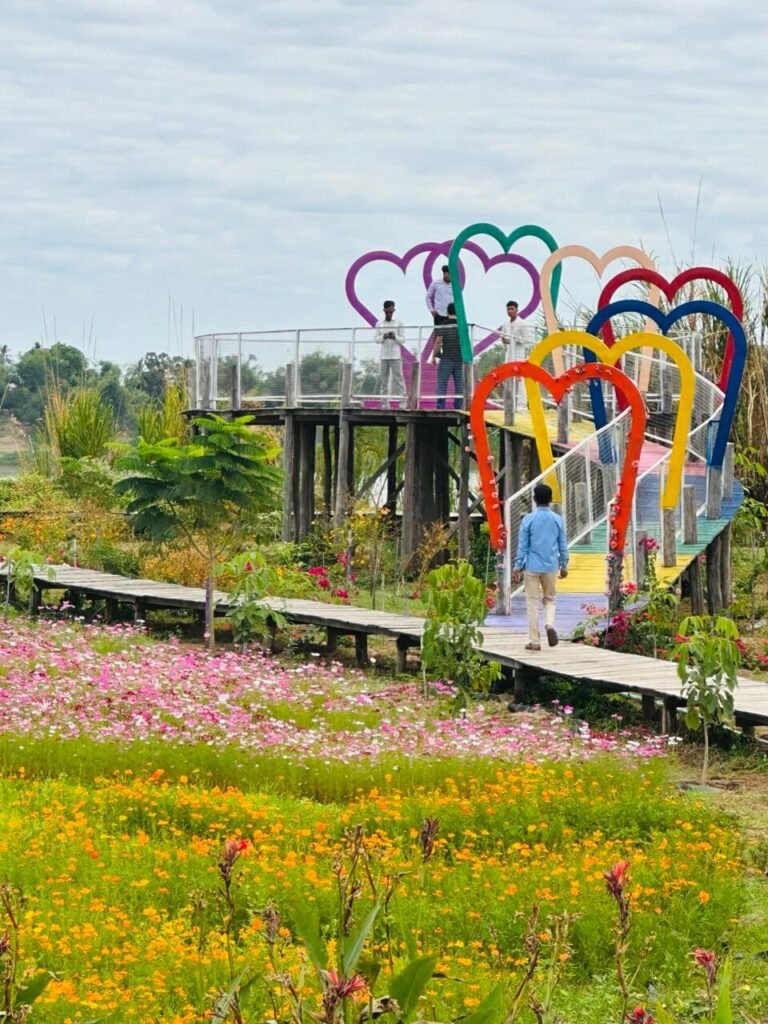 Visitors walking across the colorful heart-shaped Bridge to Heaven at a flower garden attraction.