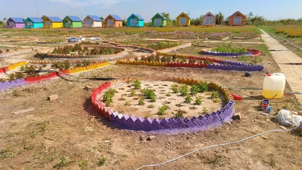 Brightly painted circular brick garden beds newly planted at Dream Garden, with colorful vacation cottages in the background.