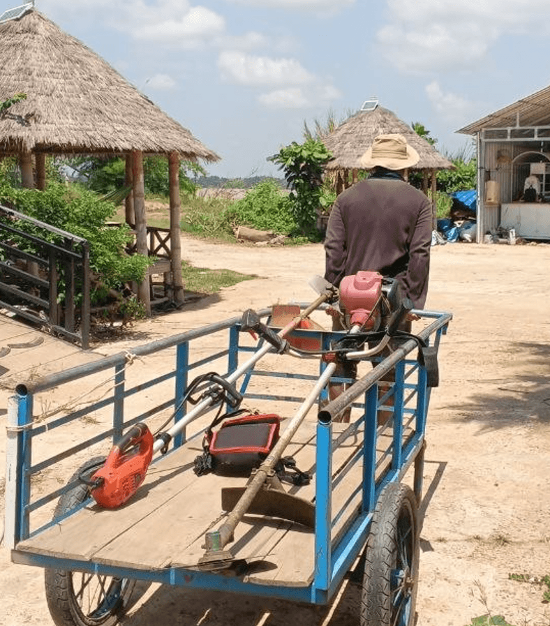 A custom blue push cart loaded with string trimmers and gardening tools on a dirt path.