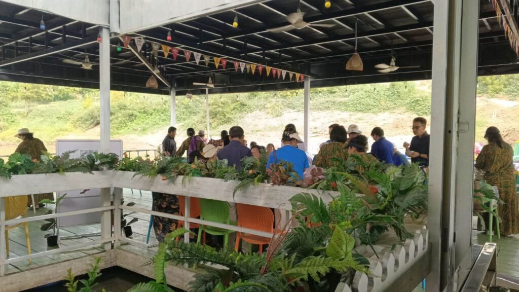 A busy waiting area filled with guests by the river at Dream Garden flower attraction.