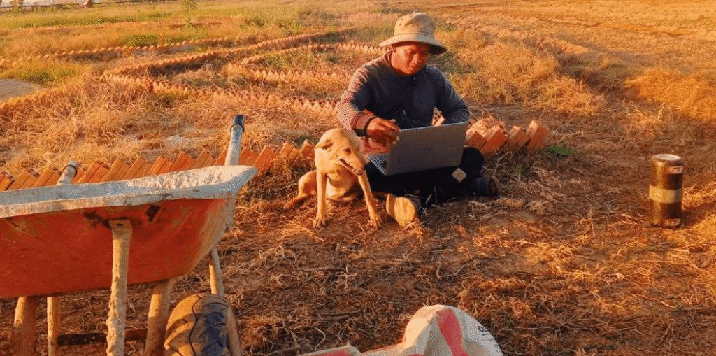 Devid Hoeur sitting on the ground with his dog and a laptop in a dry garden bed during his 2021 business failure.