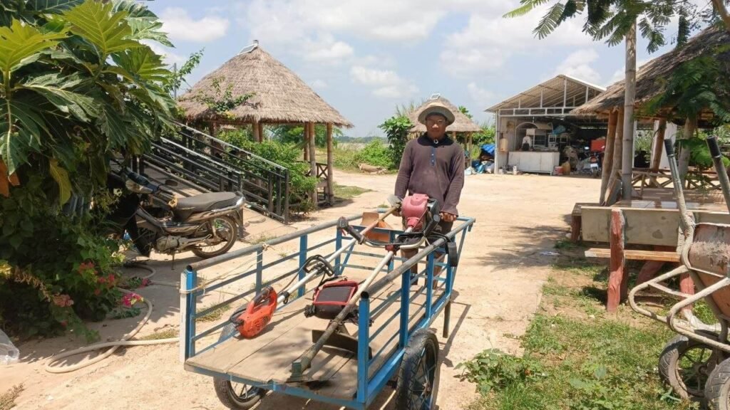 Dream Garden founder standing with his original blue pull-cart trailer loaded with grass cutting tools used to start the landscaping business.
