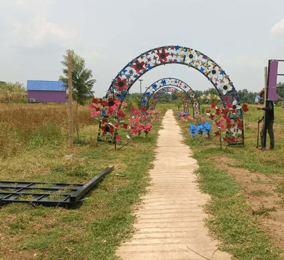 A team member working on anchoring the base of an upcycled floral garden arch along a pathway.