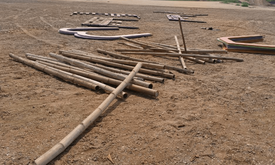Raw bamboo poles lying on the dirt ground ready for garden arch construction.
