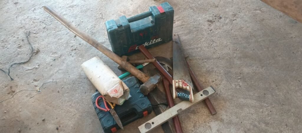 Hand tools including a saw, hammer, level, and Makita toolbox on a concrete floor.