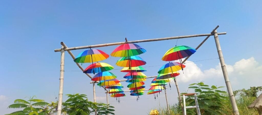 A finished hanging umbrella canopy installation creating a colorful ceiling over a garden walkway supported by natural bamboo poles.