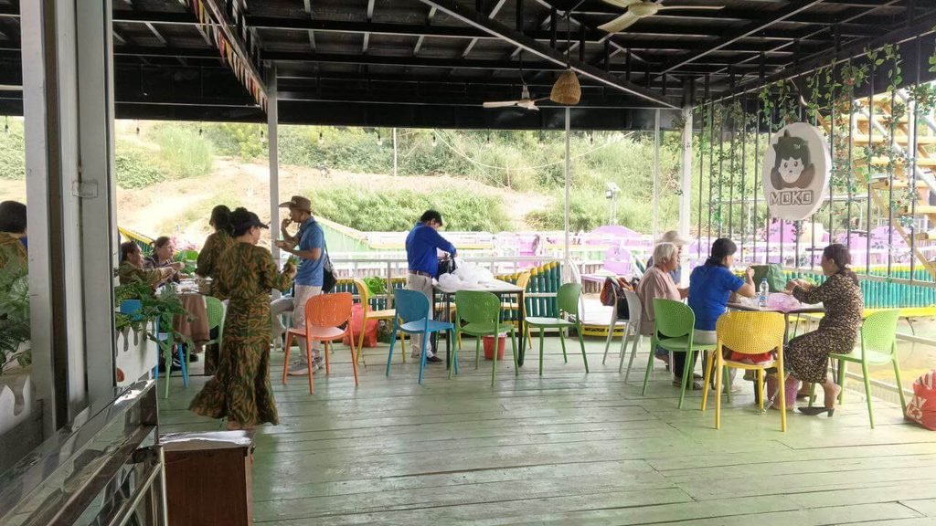 Visitors relaxing and eating in an open-air café situated next to a flower garden attraction.