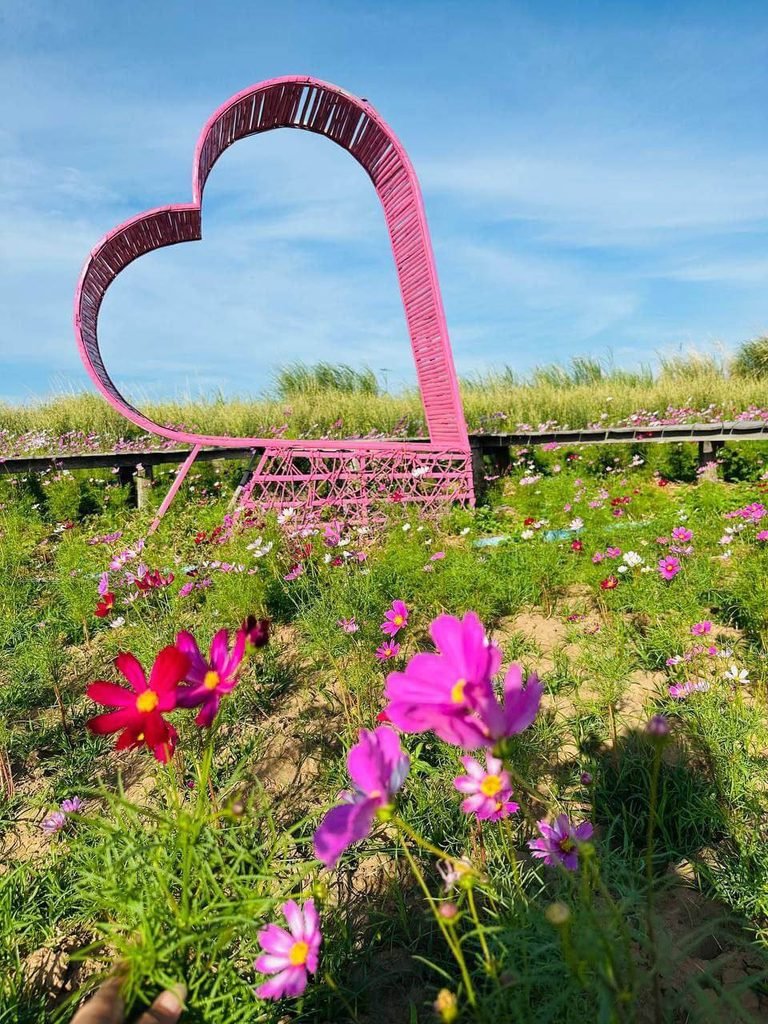 A giant pink heart landmark constructed from low-cost bamboo in the middle of a flower garden.