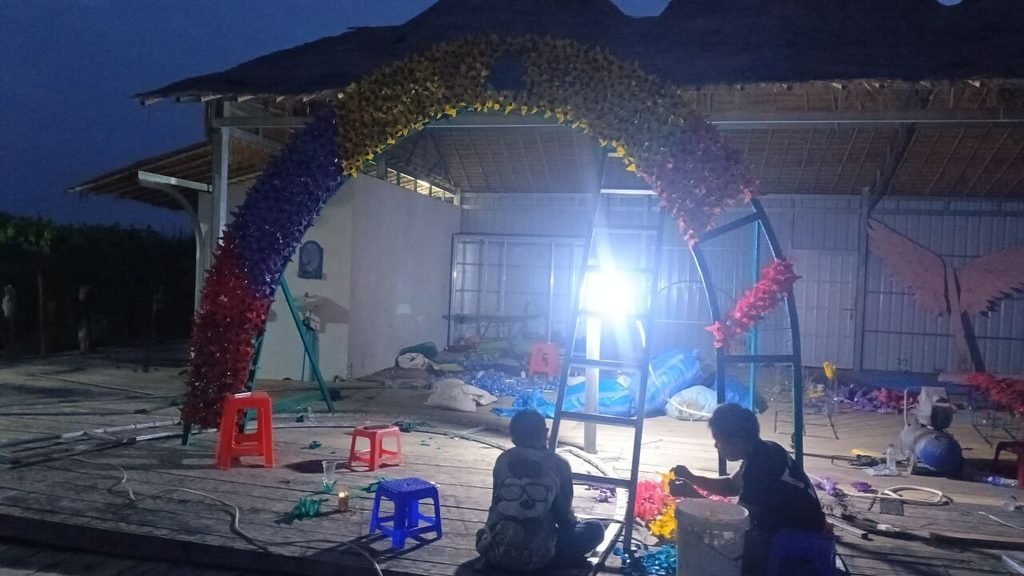 Attaching upcycled rubber flowers to a metal garden arch at night using zip ties.