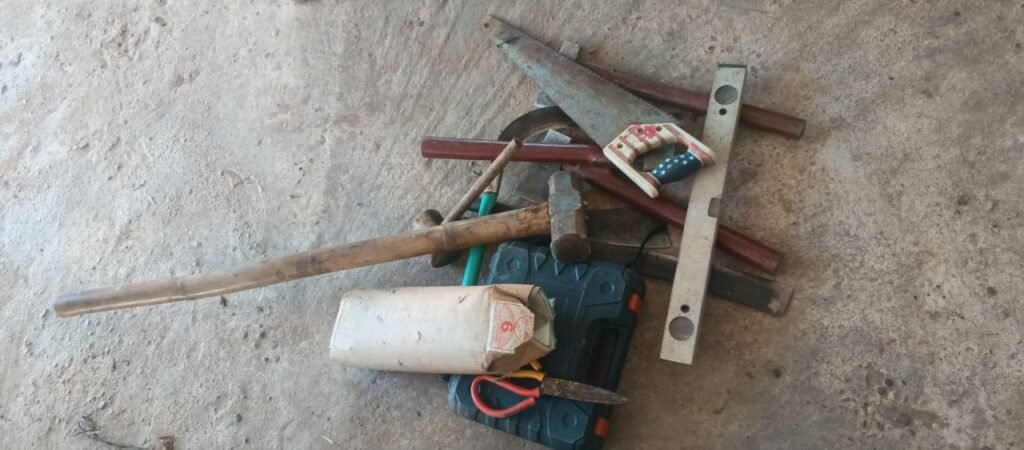Basic DIY hand tools including a hammer, saw, spirit level, and wire used to build a garden arch without welding equipment.