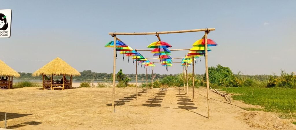 Side perspective view of a long pathway covered by a colorful hanging umbrella canopy structure in a garden setting.