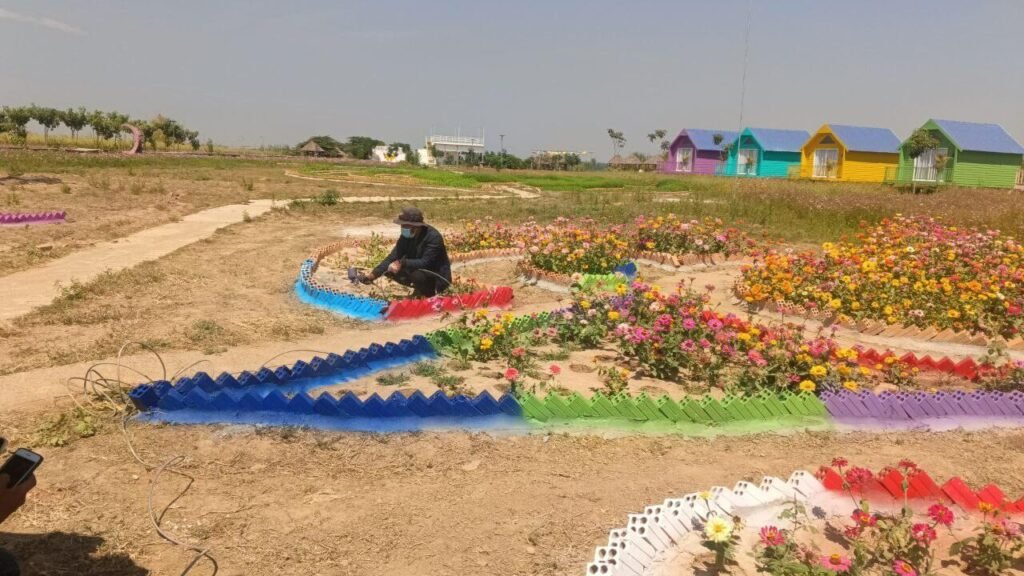 A man custom painting vertical garden brick borders in vibrant rainbow colors to match the blooming flowers and cabins.
