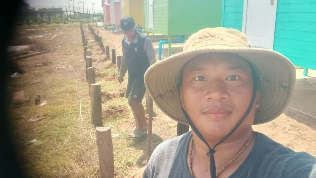 Two men setting round load-bearing wooden support posts directly into the ground for a garden boardwalk.