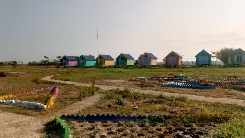 An undeveloped dirt field with colorful small cabins in the background during the early construction phase of a garden business.