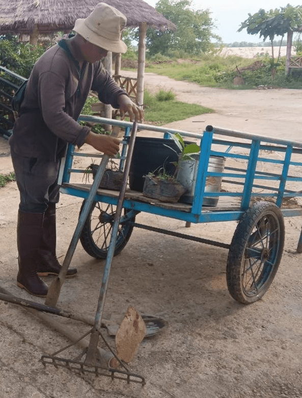 A man preparing basic gardening tools, a shovel, and a small transport cart to begin a landscaping job.