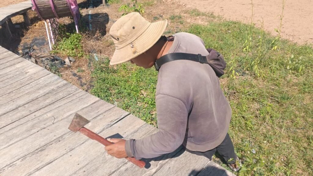 A builder using a hand axe to trim the edges of wooden decking boards on a garden walkway.