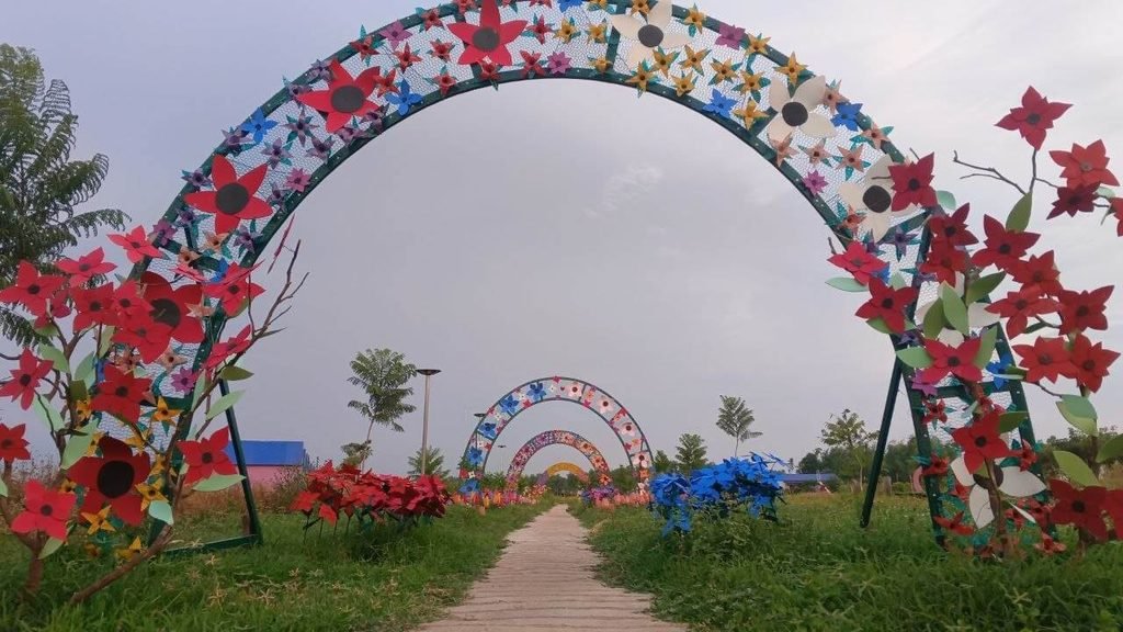 A pathway passing under a series of arched frames decorated with colorful handmade paper flowers.