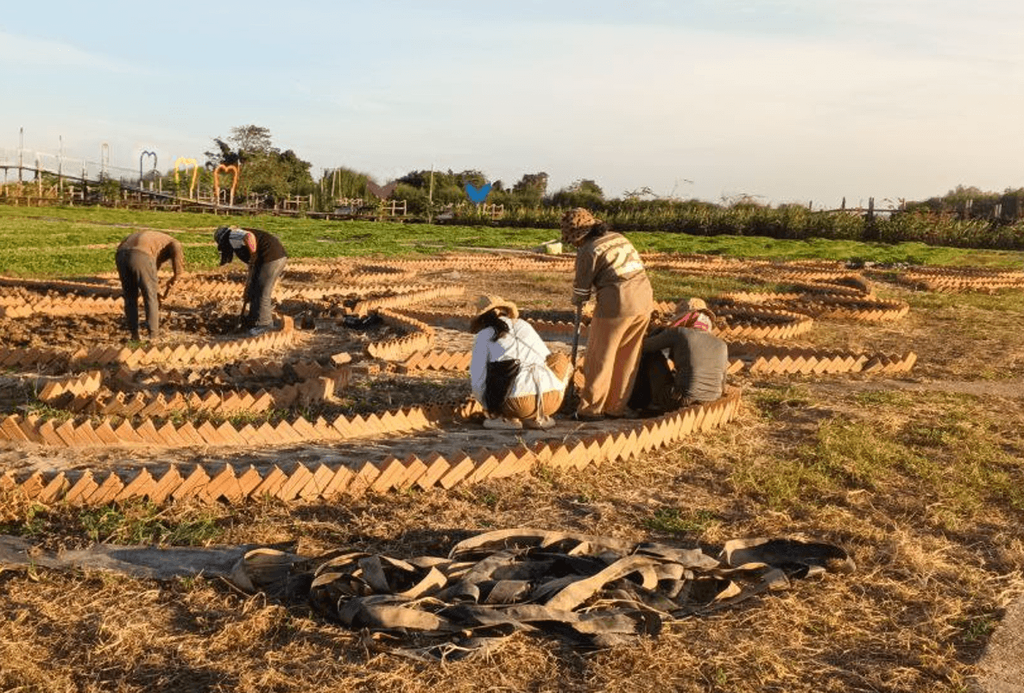 A crew hand-laying zig-zag brick borders for the first flower beds in a dirt field during the 2019 build of Dream Garden.