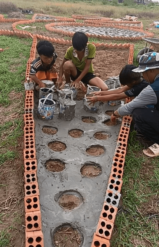 People building a garden planter on the grass using leftover bricks and discarded paint cans.