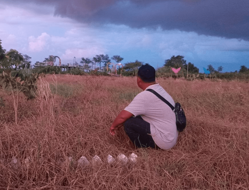 A man sitting in a dry, failed flower field at Dream Garden.