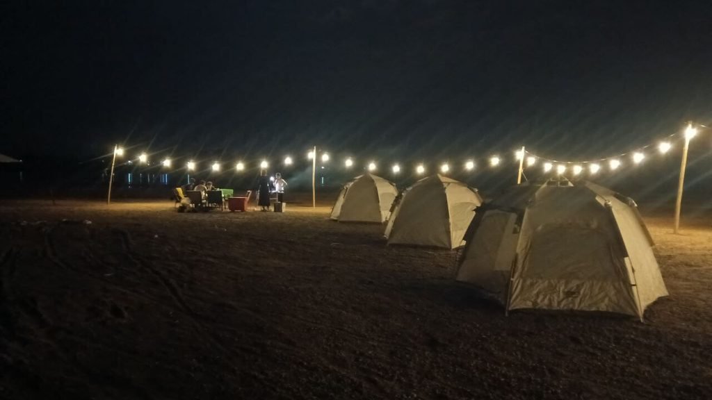 A row of camping dome tents set up at night under glowing string lights at the flower attraction.