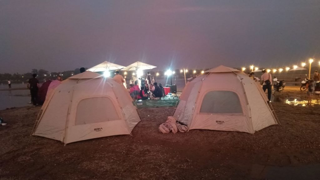 Two glamping tents illuminated at dusk with guests gathering on the beach in the background at Dream Garden.