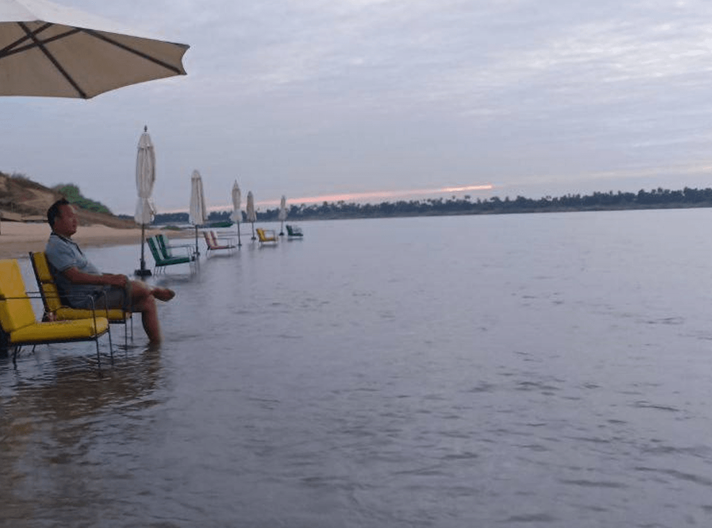 A man sitting on a yellow chair in the shallow water under an umbrella in Preah Sihanouk.